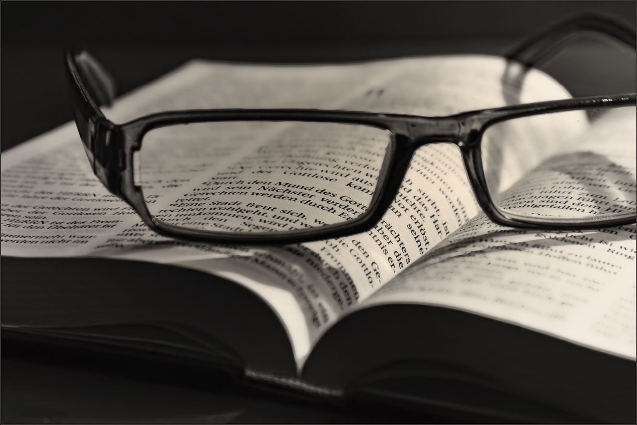 Artistic black and white image of eyeglasses resting on an open book. Ideal for literature or vision concepts.